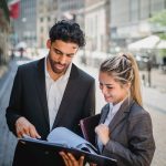Young business professionals in formal attire reviewing documents outdoors, showcasing teamwork.