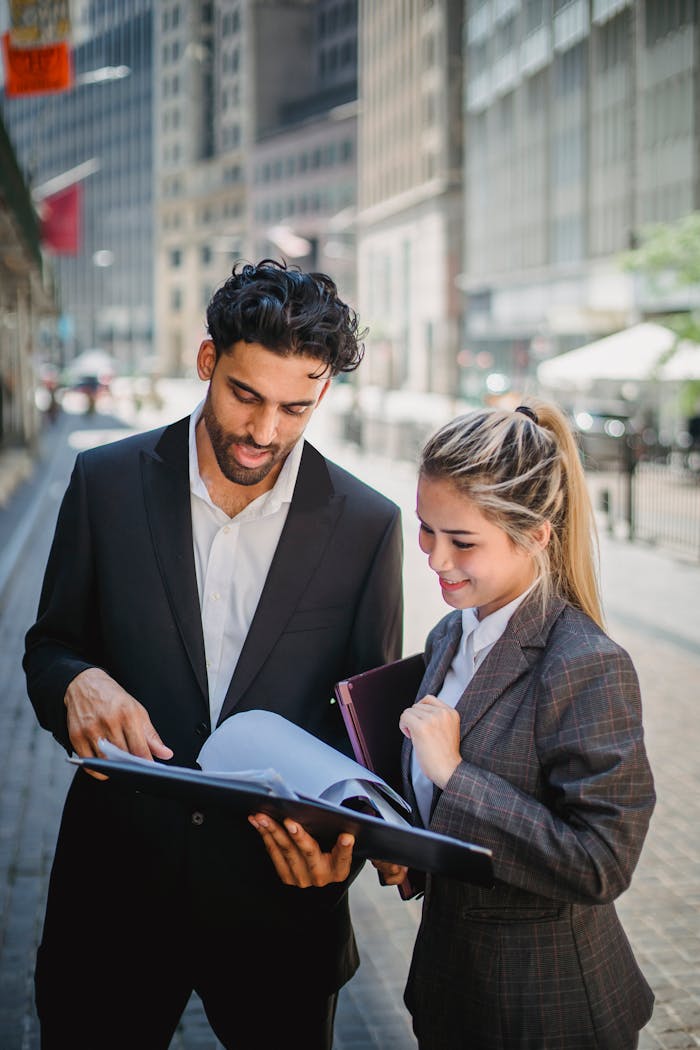 Young business professionals in formal attire reviewing documents outdoors, showcasing teamwork.