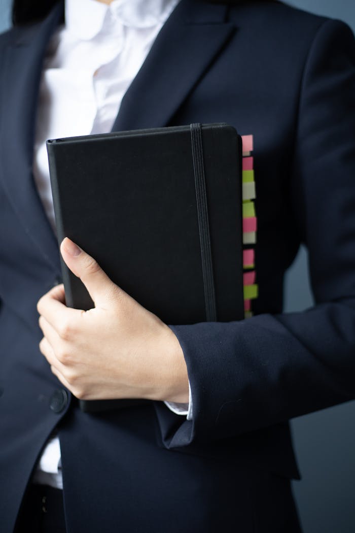A businesswoman in a suit holds a planner with colorful tabs in an office setting.