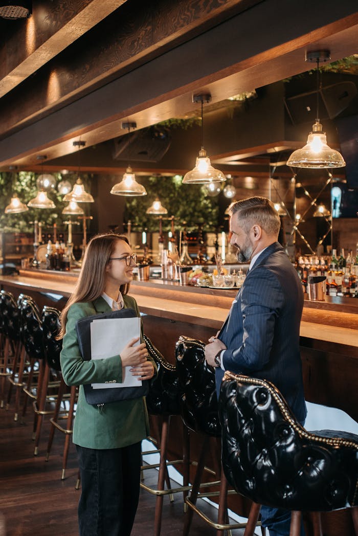 about-img-01 Two professionals engage in a business discussion at a stylish bar with modern design elements.
