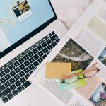 The Art of Drawing Readers In: Your attractive post title goes here A top view of travel planning essentials on a laptop with a map, credit cards, and a magazine.